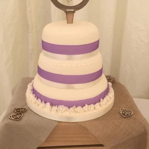 A 3 tiered celebration cake with purple ribbon decorations.